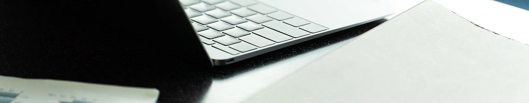 机上でノートパソコンのキーボードと資料が並ぶ、ビジネスニュースヘッダー用イメージ