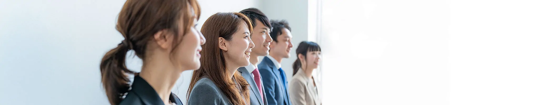スーツ姿の男女数名が横一列に並び、笑顔で前方を見つめる採用向け企業イメージ写真