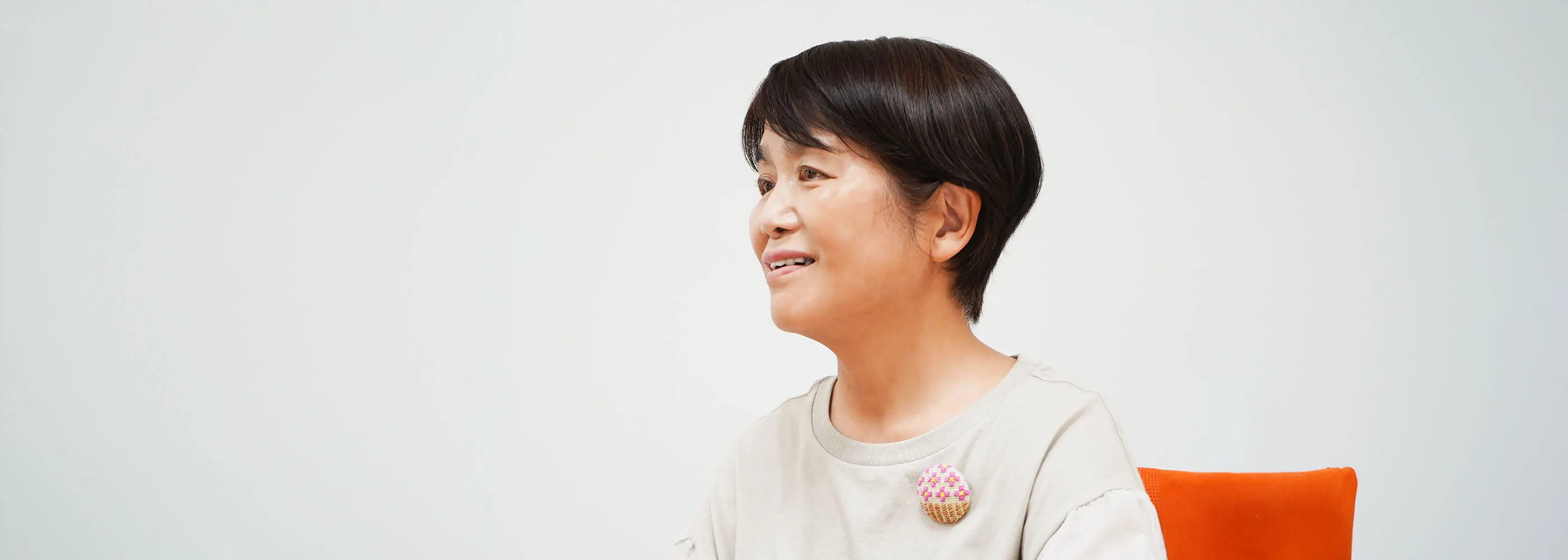 白いオフィスで淡色トップスの女性が横顔で微笑みながら話すインタビューシーン